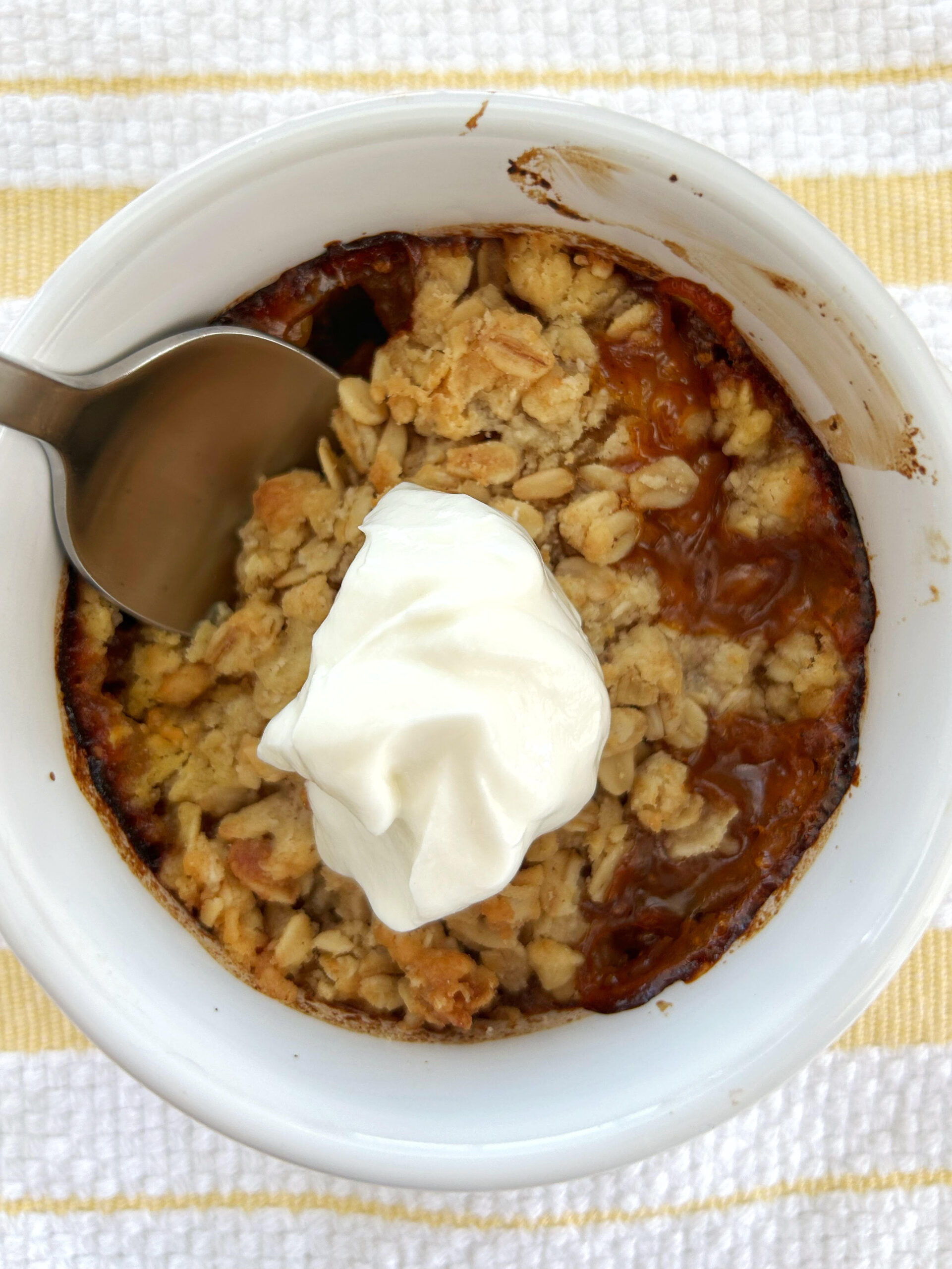 Mango crisp dessert topped with a dollop of yogurt in a white bowl with a yellow and white striped background