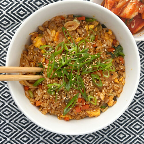 Fried rice with kimchi topped with green onion in a white bowl with a black and white patterned background