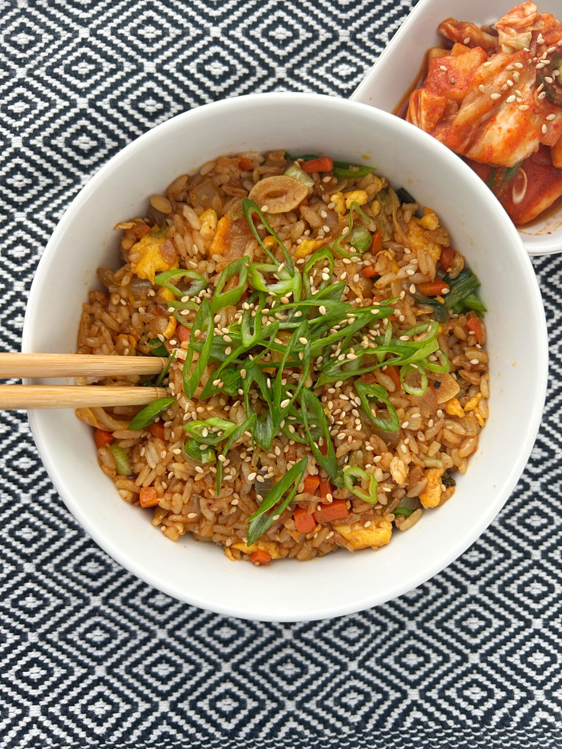 Fried rice with kimchi topped with green onion in a white bowl with a black and white patterned background