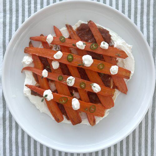 Roasted carrots with matbucha and whipped goat cheese on a white plate with a striped background
