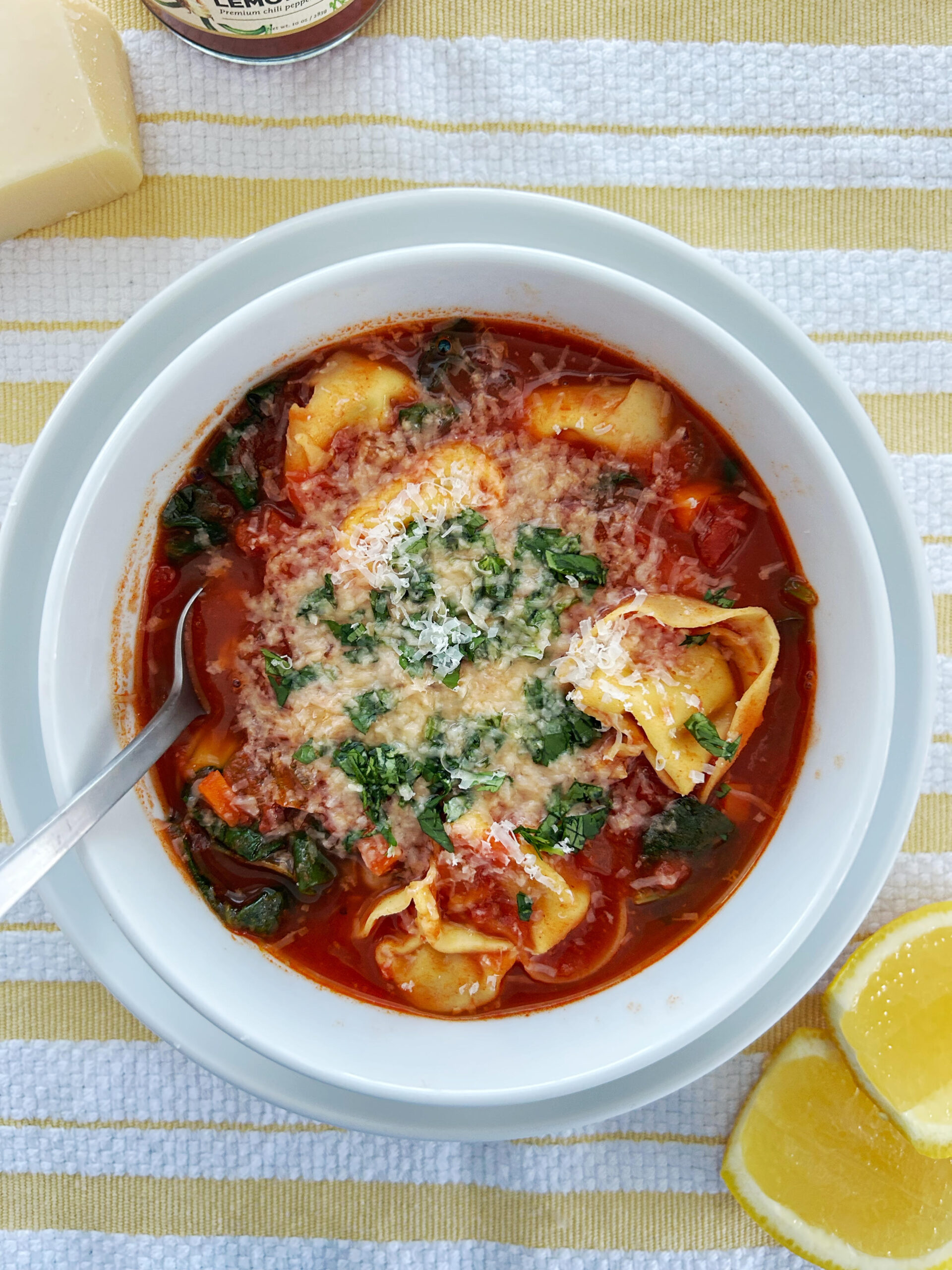 spicy harissa tortellini soup in a white bowl with a white and yellow striped background